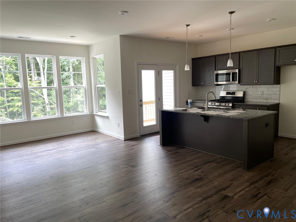 Kitchen with backsplash, dark hardwood / wood-style floors, a kitchen island with sink, appliances with stainless steel finishes, and dark stone countertops