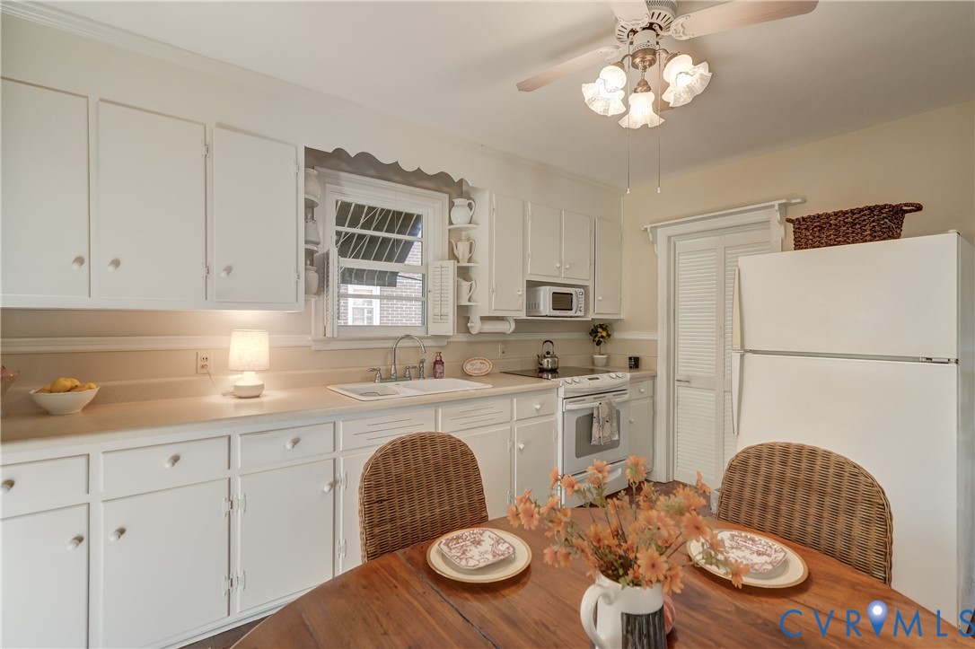 Kitchen featuring white shaker-style cabinetry, solid-surface countertops, dual-basin sink, overhead ceiling fan with light fixture, and louvered door closet