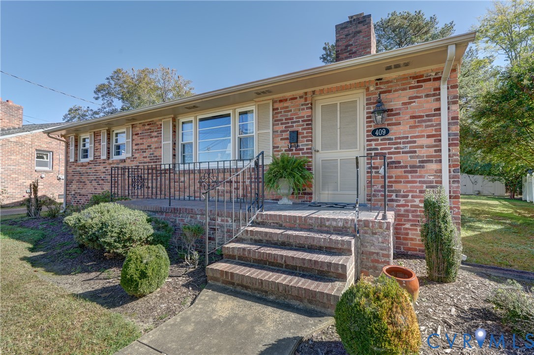 Brick exterior featuring a multi-pane window configuration, covered entryway, masonry chimney, and metal railings