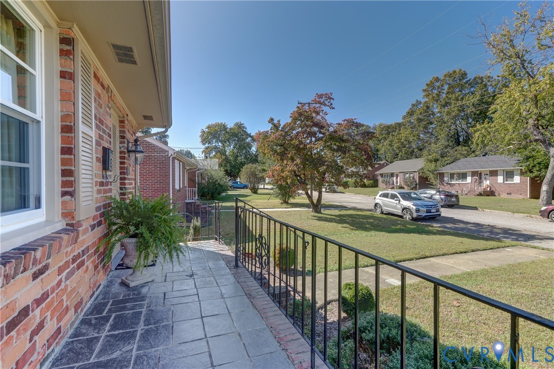 Exterior covered porch featuring brick masonry siding, flagstone flooring, and black wrought-iron railing