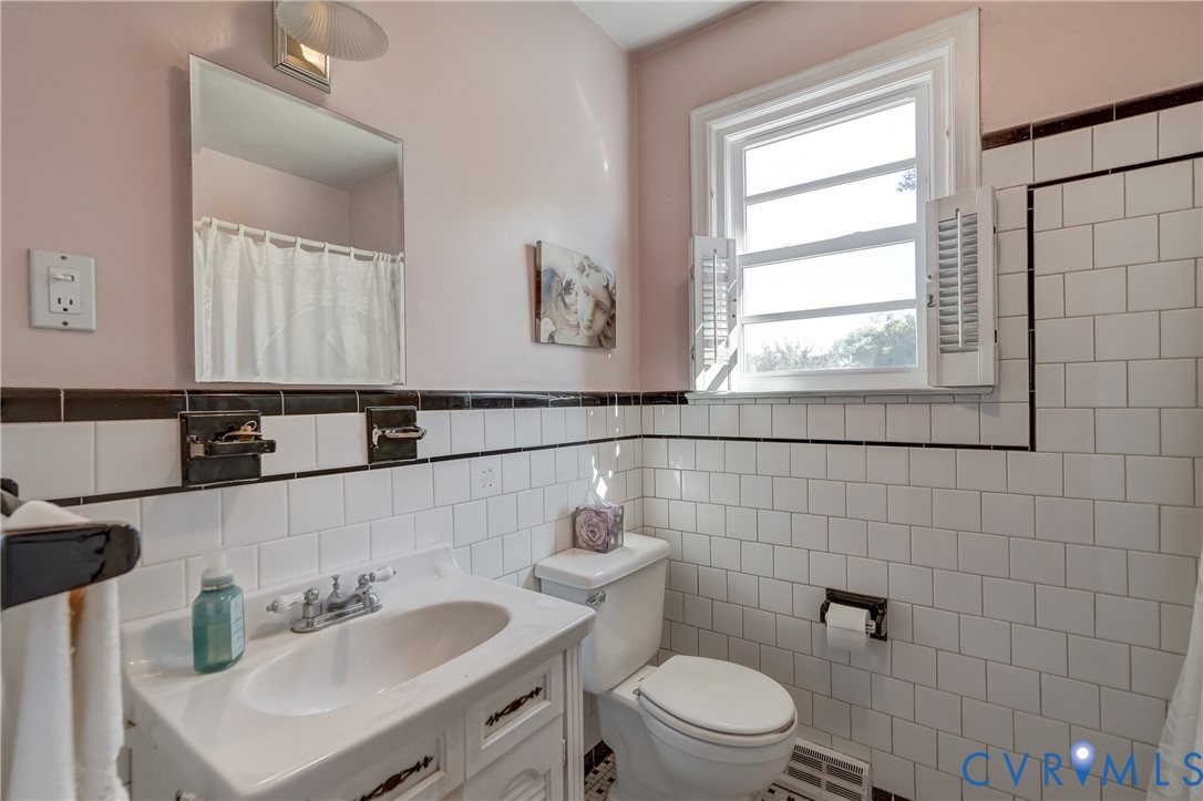 Bathroom featuring white wall tile with black trim, a vanity with an integrated sink, polished metal faucet hardware, and a window with plantation shutters