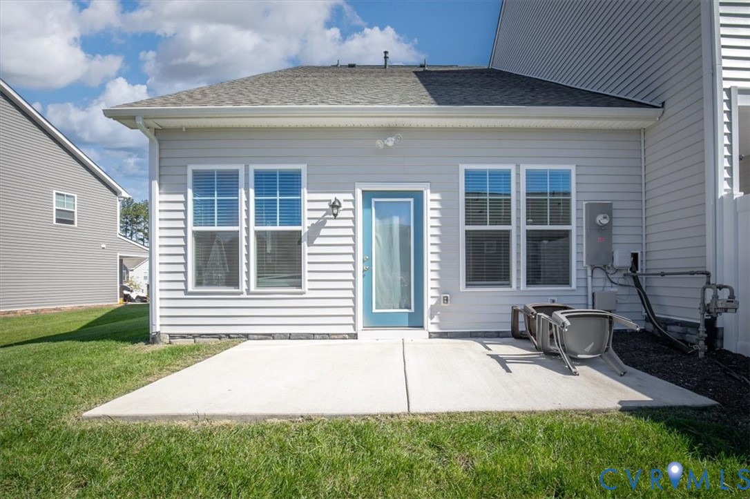 Rear exterior featuring light-colored horizontal siding, a concrete patio, four double-hung windows, and a glass-paneled entry door