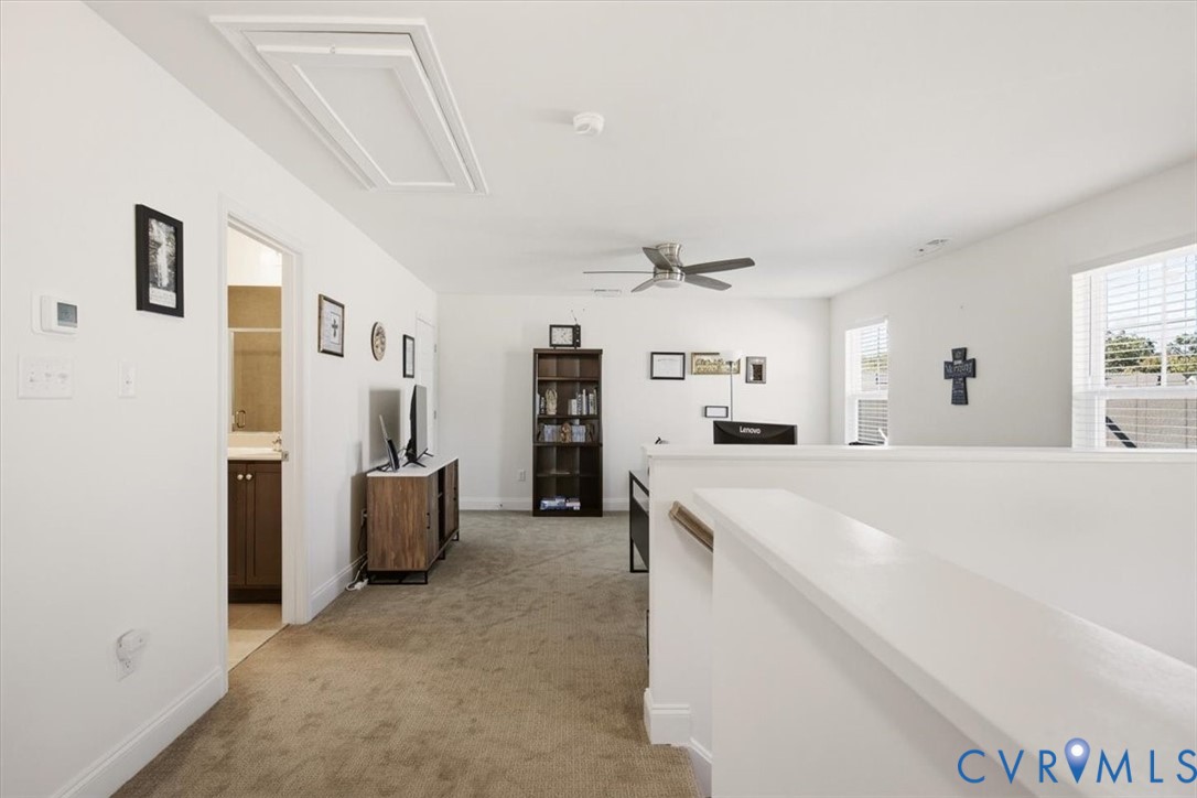 Open floor area with neutral carpeting, ceiling fan, dual windows, and access to a bathroom