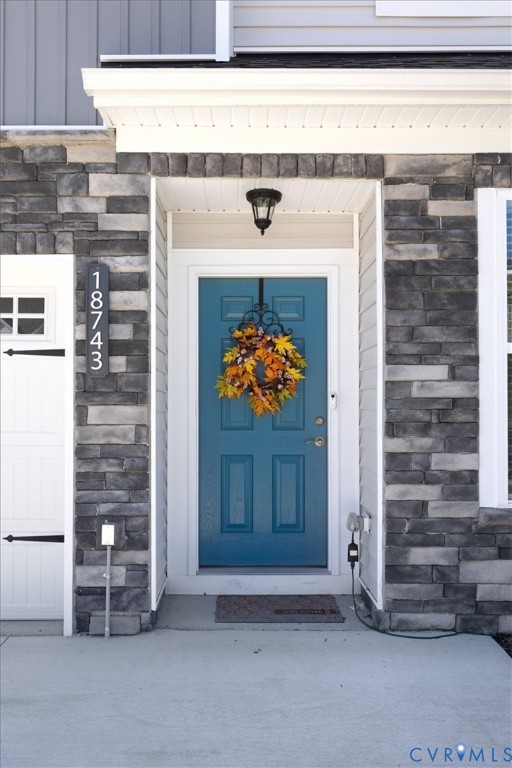 Covered entryway featuring a stone veneer facade, a panelized door with a metallic handle set, and a built-in overhead light fixture