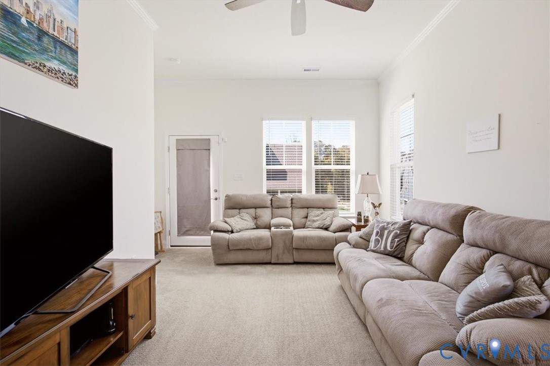 High ceilings with a central ceiling fan, neutral carpeting, and abundant natural light from multiple windows and a glass-paneled exterior door