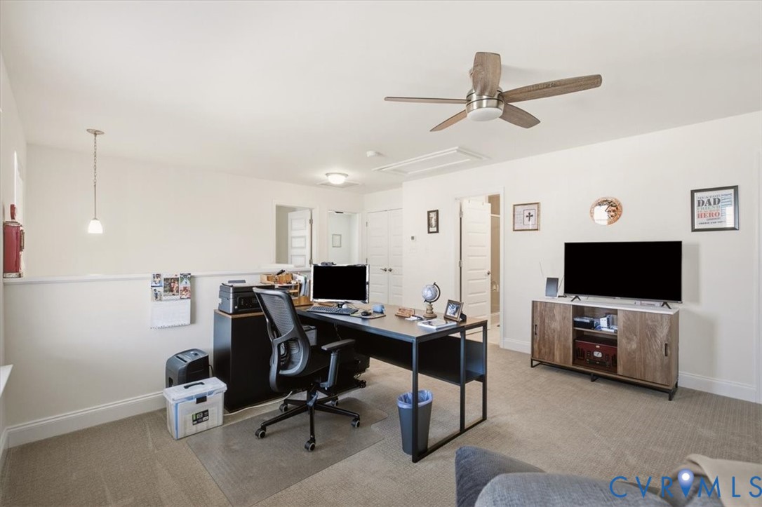 Multi-purpose room featuring neutral carpeting, a ceiling fan with integrated lighting, a pendant light fixture, and interior doors