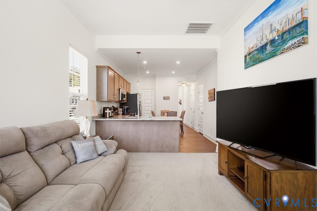 Open-concept interior featuring light-toned carpeting, wood-finish flooring, kitchen cabinetry, and a peninsula-style breakfast bar with stone-surface countertop