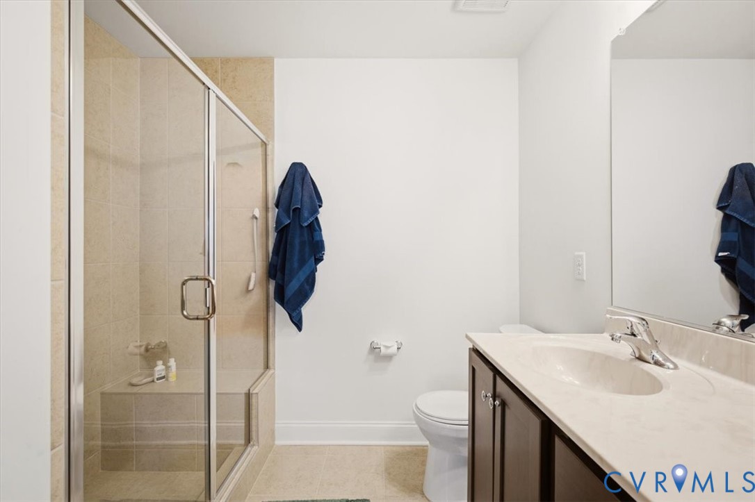 Bathroom featuring a glass-enclosed shower with tile surround and integrated bench, dark wood-finish cabinetry, solid-surface countertop with integrated sink, and full-width wall mirror