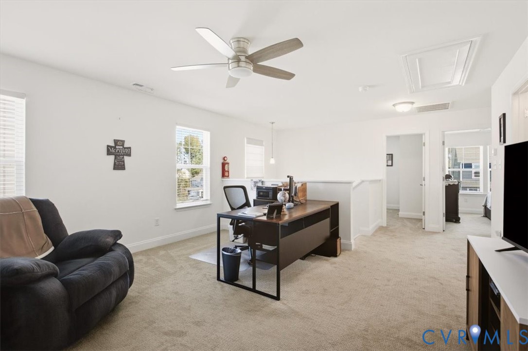 Neutral-toned carpeted flooring, brushed metal ceiling fan, and multiple windows providing natural light