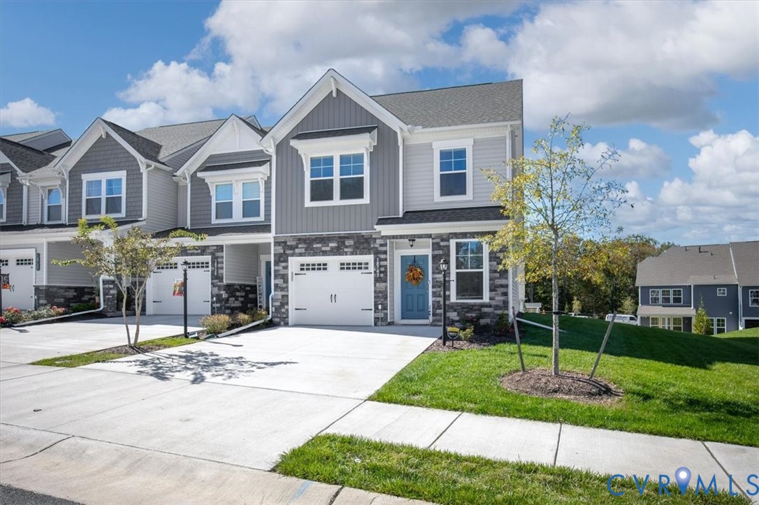 Multi-level townhome exterior featuring gray horizontal siding, stone veneer accents, an attached single-car garage, and asphalt shingle roofing