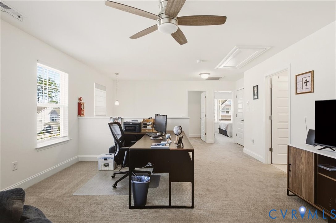 Neutral-toned interior space featuring wall-to-wall carpeting, a ceiling fan with integrated lighting, dual-pane windows, and multi-panel interior doors