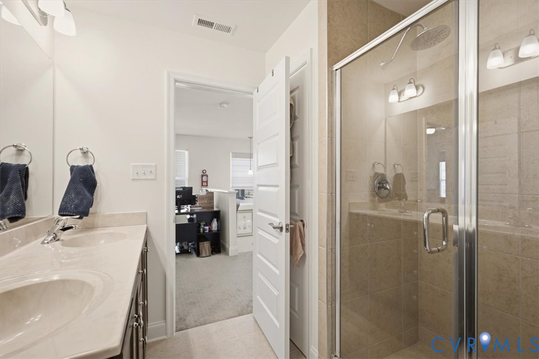 Bathroom featuring a dual-sink vanity with a stone-surface countertop, a glass-enclosed walk-in shower with tile surround, and an integrated lighting fixture