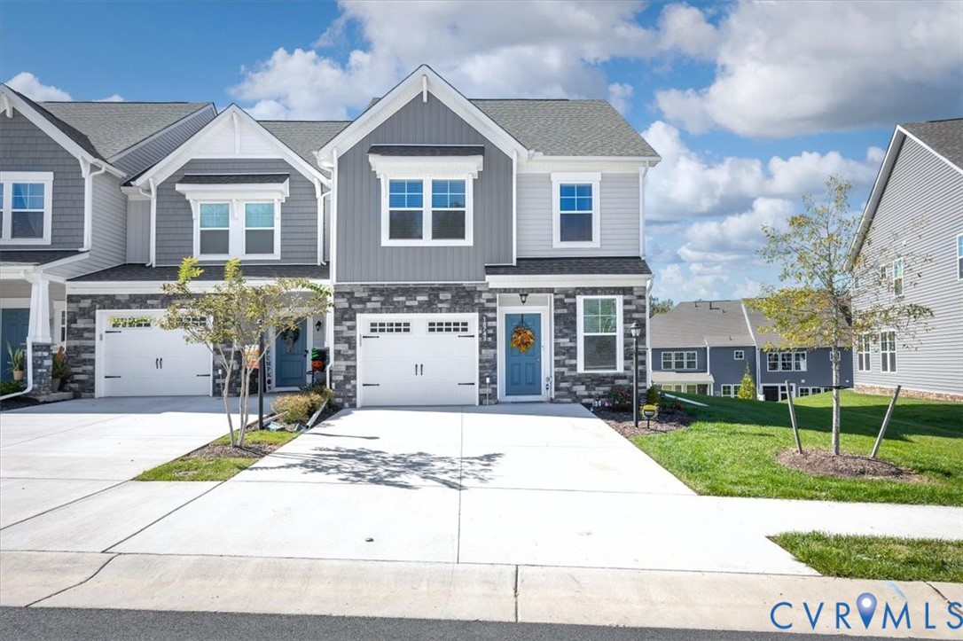 Two-story exterior featuring stone veneer siding, dual-pane windows, a paved concrete driveway, and an attached two-car garage