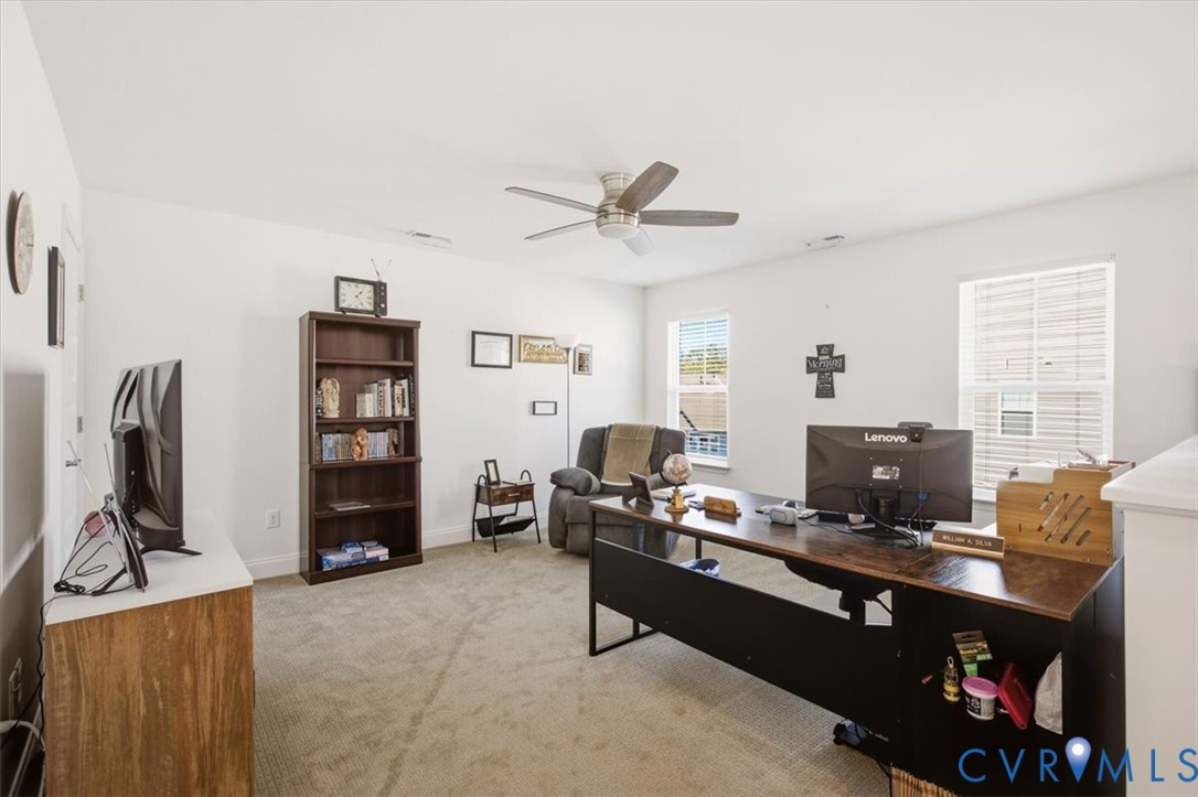 Neutral-toned wall-to-wall carpeting, ceiling fan with integrated lighting, and multiple windows providing natural light