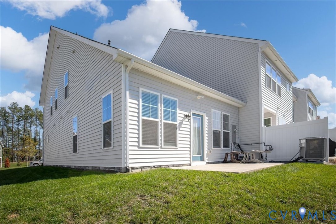 Rear exterior featuring light gray horizontal siding, a concrete patio, multi-pane windows, and a white privacy fence