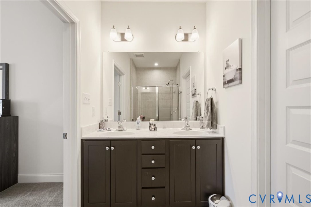 Dark cabinetry vanity with a stone countertop, dual undermount sinks, two-light wall-mounted fixtures, and an oversized frameless mirror