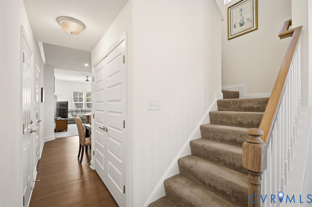 Entryway featuring wood-finish flooring, a double-door closet, and a staircase with a wooden handrail and white balusters