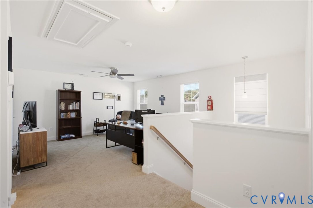 Open-concept space featuring neutral carpeting, a ceiling fan with integrated lighting, a flush-mount ceiling light, and a staircase with a handrail
