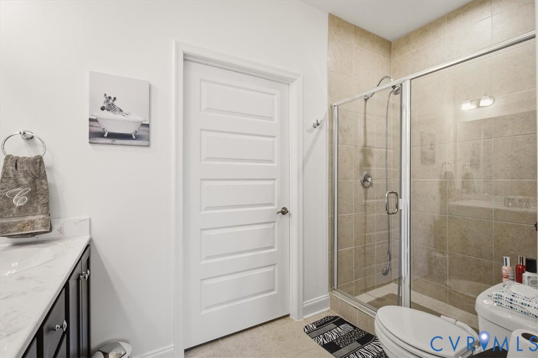 Bathroom featuring a vanity with stone-finish countertop and undermount sink, a tiled walk-in shower with glass enclosure, and a five-panel interior door