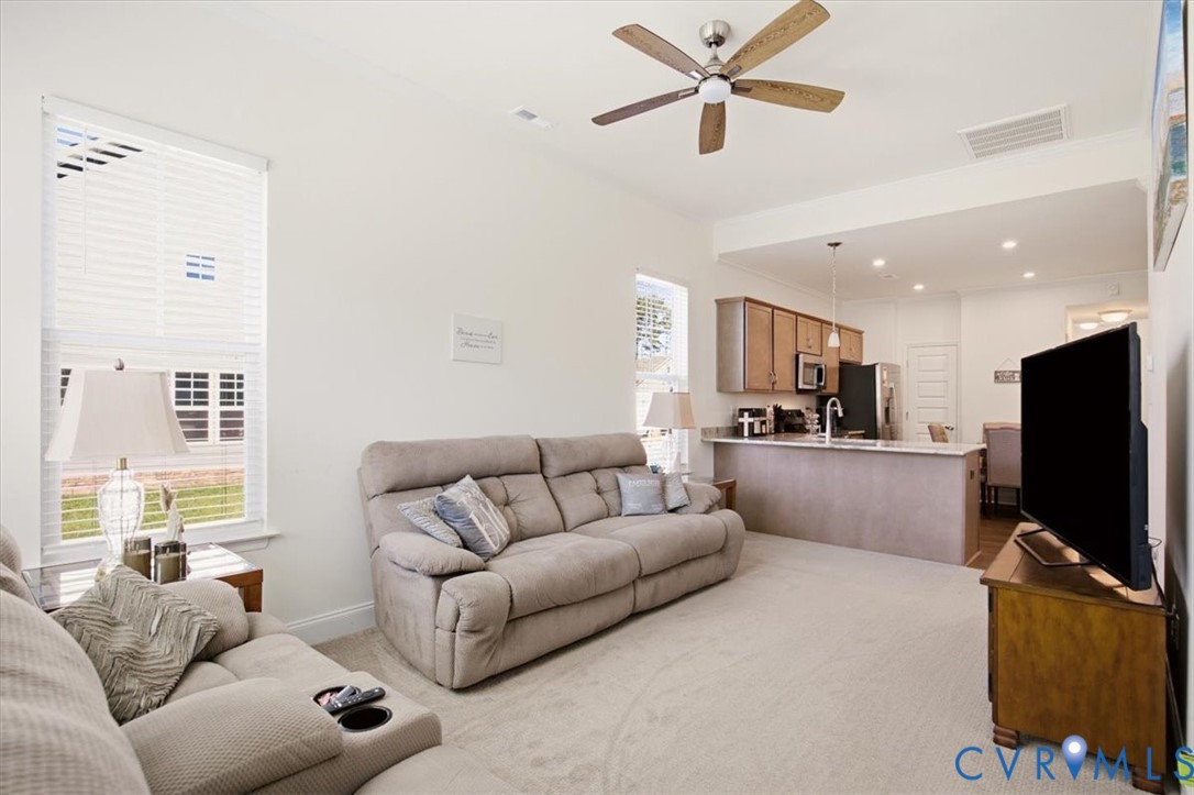 Open-concept interior featuring a breakfast bar with stone-surface countertop, cabinetry with brushed-metal hardware, ceiling fan with light fixture, and windows with horizontal blinds