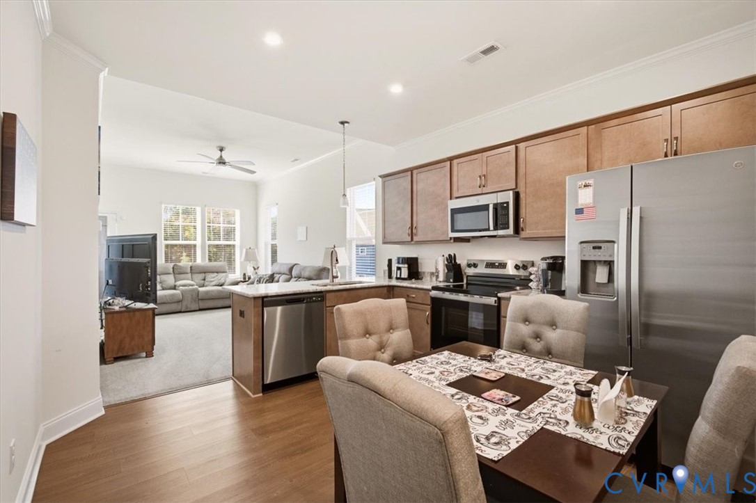 Kitchen featuring wood-finish cabinetry, stone-style countertops, stainless steel appliances, a peninsula breakfast bar, and recessed lighting