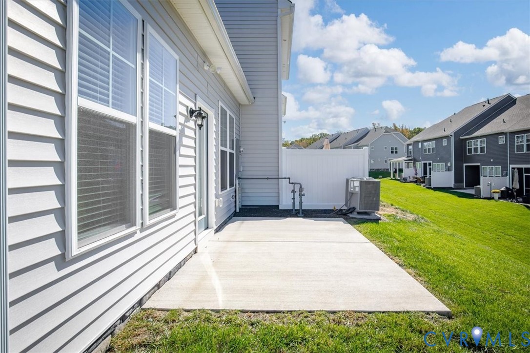 Exterior elevation featuring light-colored horizontal lap siding, a concrete patio, and a white vinyl privacy fence