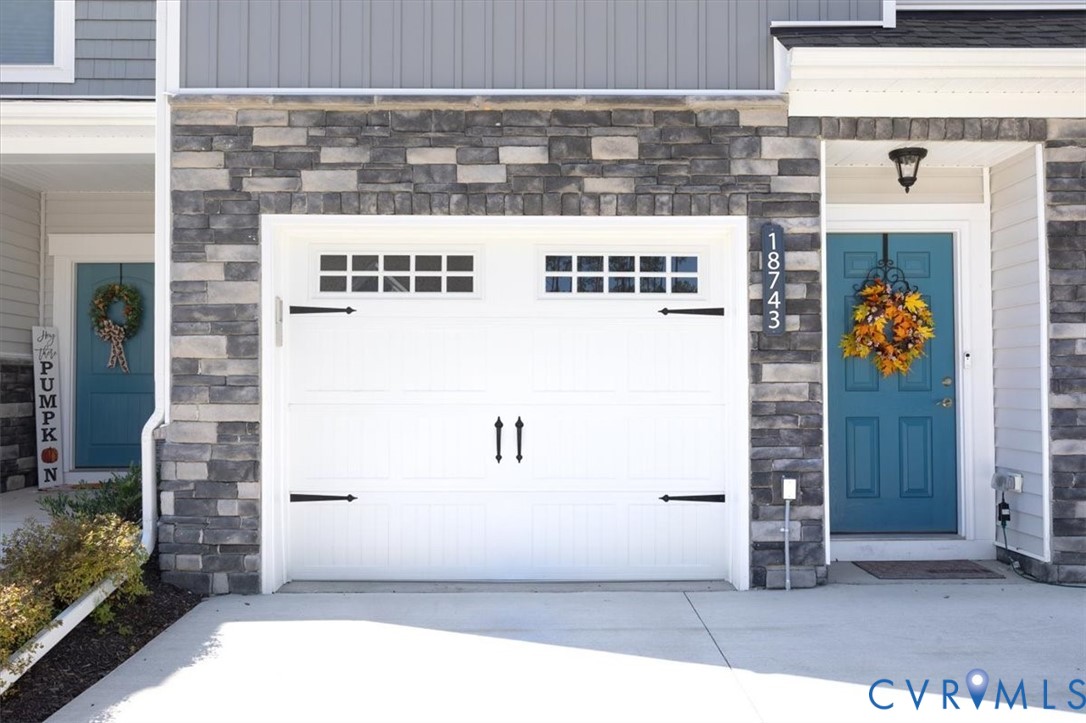 Exterior facade featuring stacked stone veneer, white garage door with decorative hardware and transom windows, and teal-painted entry door