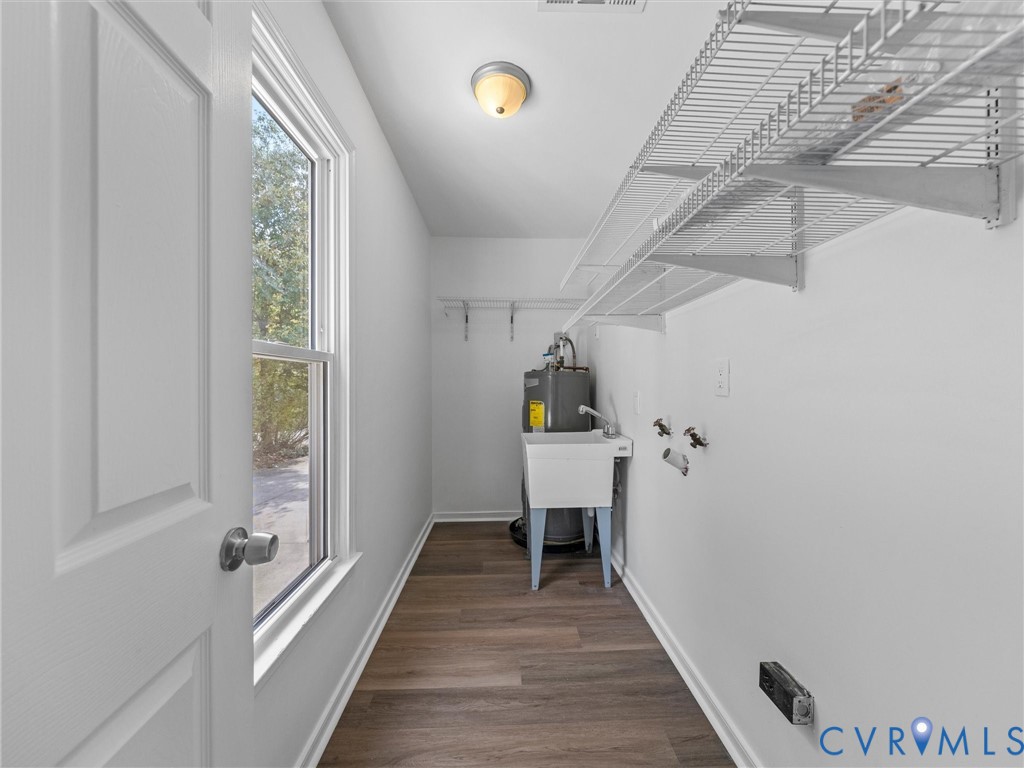 Utility room featuring wood-finish flooring, a wall-mounted wire shelving system, a freestanding utility sink, and a flush-mount ceiling light fixture