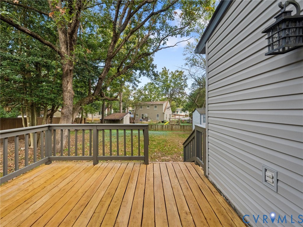 Wood-plank deck featuring dark-toned railings, horizontal vinyl siding, and an attached exterior wall-mounted lantern