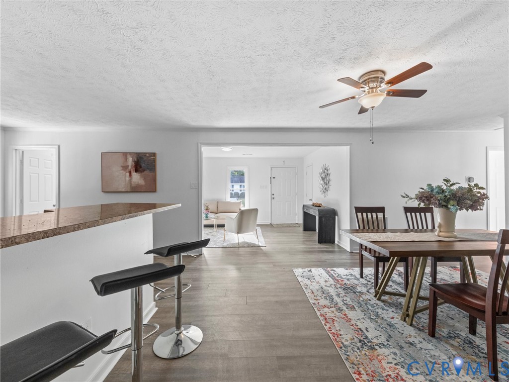 Open concept interior featuring wood-finish flooring, breakfast bar with stone-surfaced countertop, and ceiling fan with integrated lighting