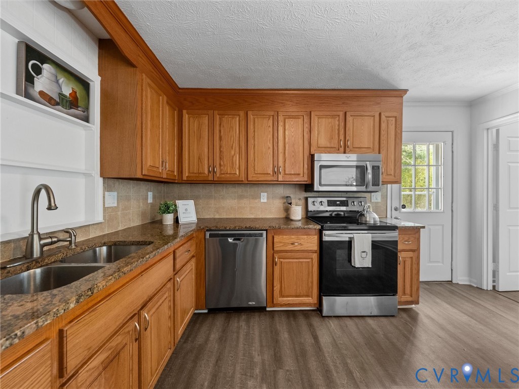 Kitchen featuring wood cabinetry, stone-finish countertops, stainless steel appliances, and wood-finish flooring