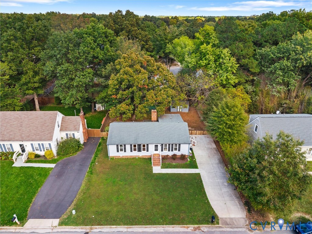 Single-story residence featuring a shingled roof, exterior brick chimney, concrete driveway, and mature landscaping on a tree-lined lot