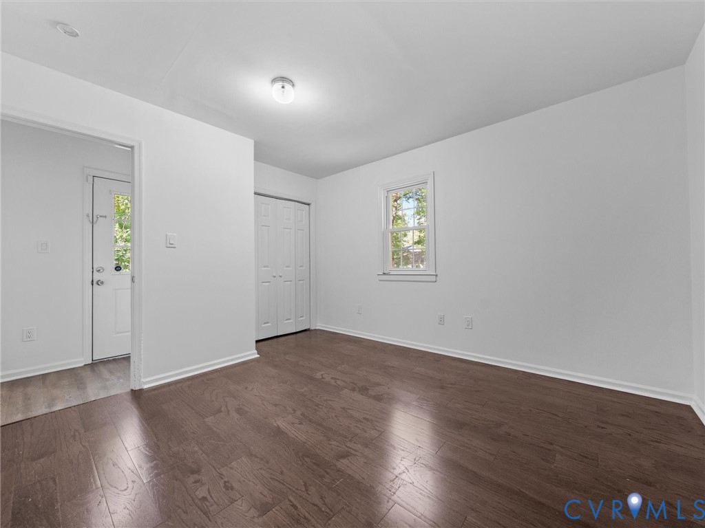 Interior room featuring wood-finish flooring, a single window with white trim, and a built-in closet with bi-fold doors