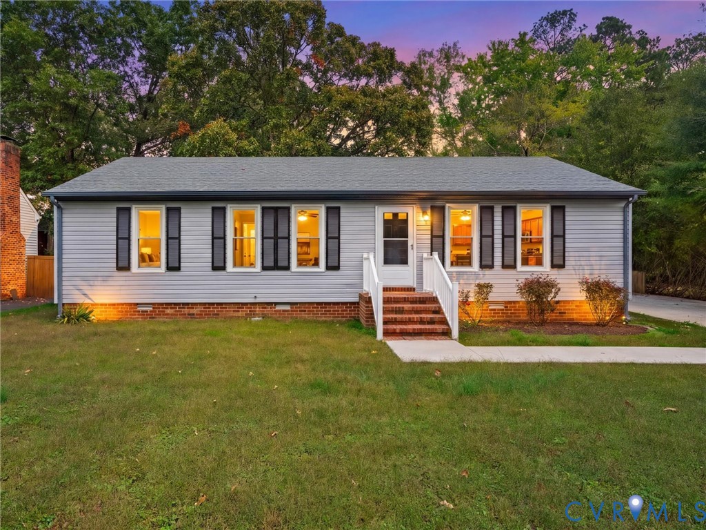 Single-story exterior featuring horizontal siding, dark decorative shutters, brick foundation trim, and a brick front stoop with a white railing