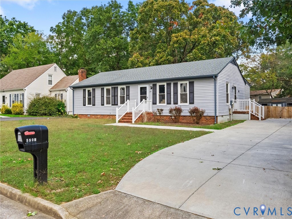Single-story exterior featuring light-gray horizontal siding, dark shutters, a brick foundation, white railings, and a concrete driveway Single-story exterior featuring light-gray horizontal siding, dark shutters, a brick foundation, white railings, and a concrete driveway