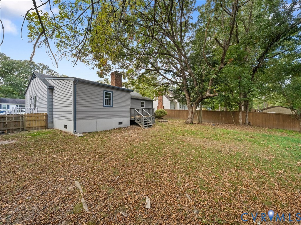 Rear exterior featuring light-colored horizontal siding, a wood-frame deck with stairs, a brick chimney, and a full-perimeter privacy fence