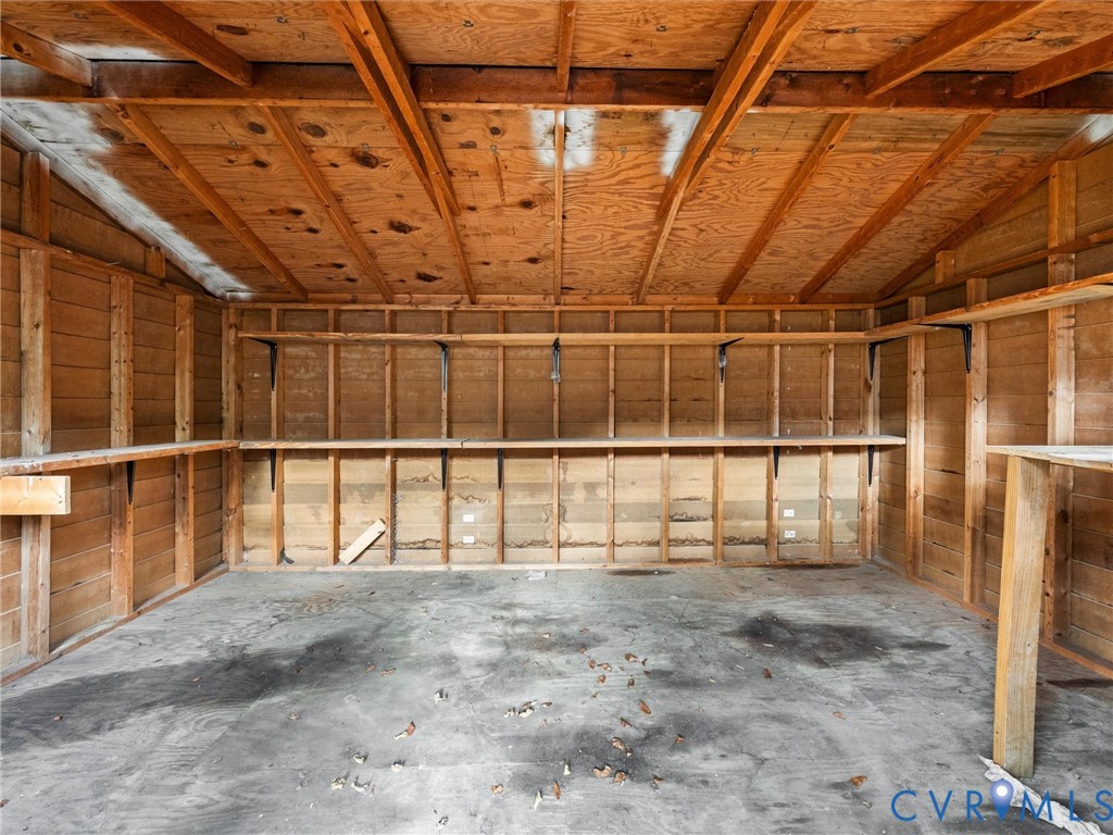 Enclosed storage structure featuring exposed timber framing, concrete flooring, and multiple built-in wood-plank shelving units
