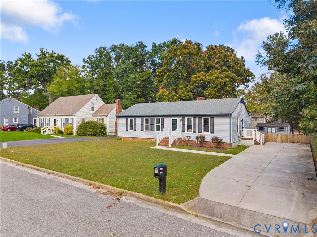 Single-story residence featuring horizontal lap siding, a shingled roof, dark louvered shutters, an attached concrete driveway, and a fenced exterior storage structure Single-story residence featuring horizontal lap siding, a shingled roof, dark louvered shutters, an attached concrete driveway, and a fenced exterior storage structure