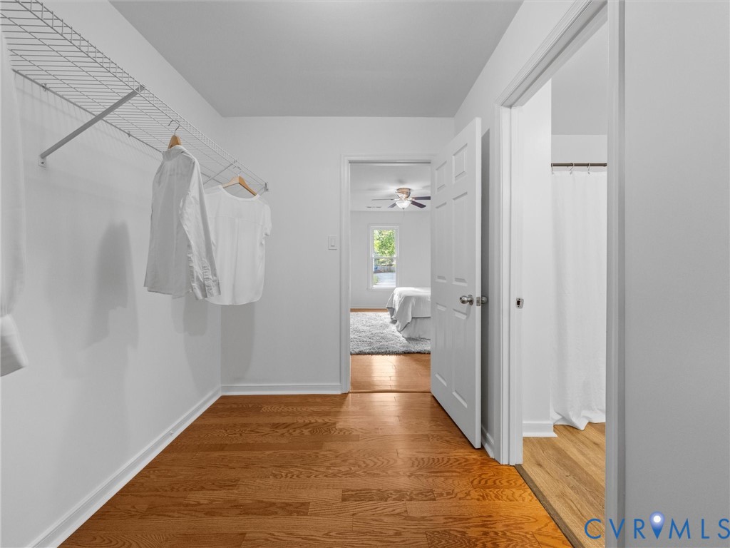 Walk-in closet featuring wood-finish flooring and wire shelving, with a six-panel door opening into a tiled floor bathroom