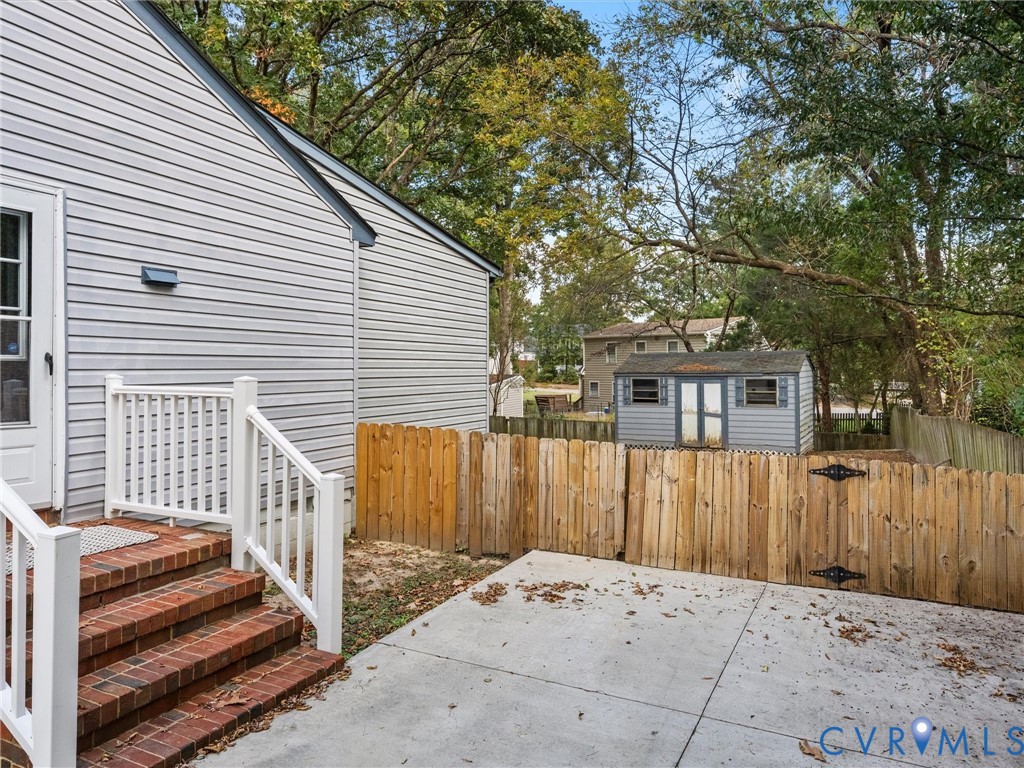 Exterior area featuring a concrete patio, red brick steps, white railing, wood fence, and a detached storage structure