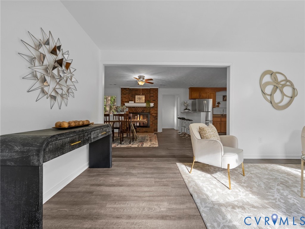 Wood-finish flooring throughout, brick fireplace with a white mantel, and ceiling fan with integrated lighting Wood-finish flooring throughout, brick fireplace with a white mantel, and ceiling fan with integrated lighting