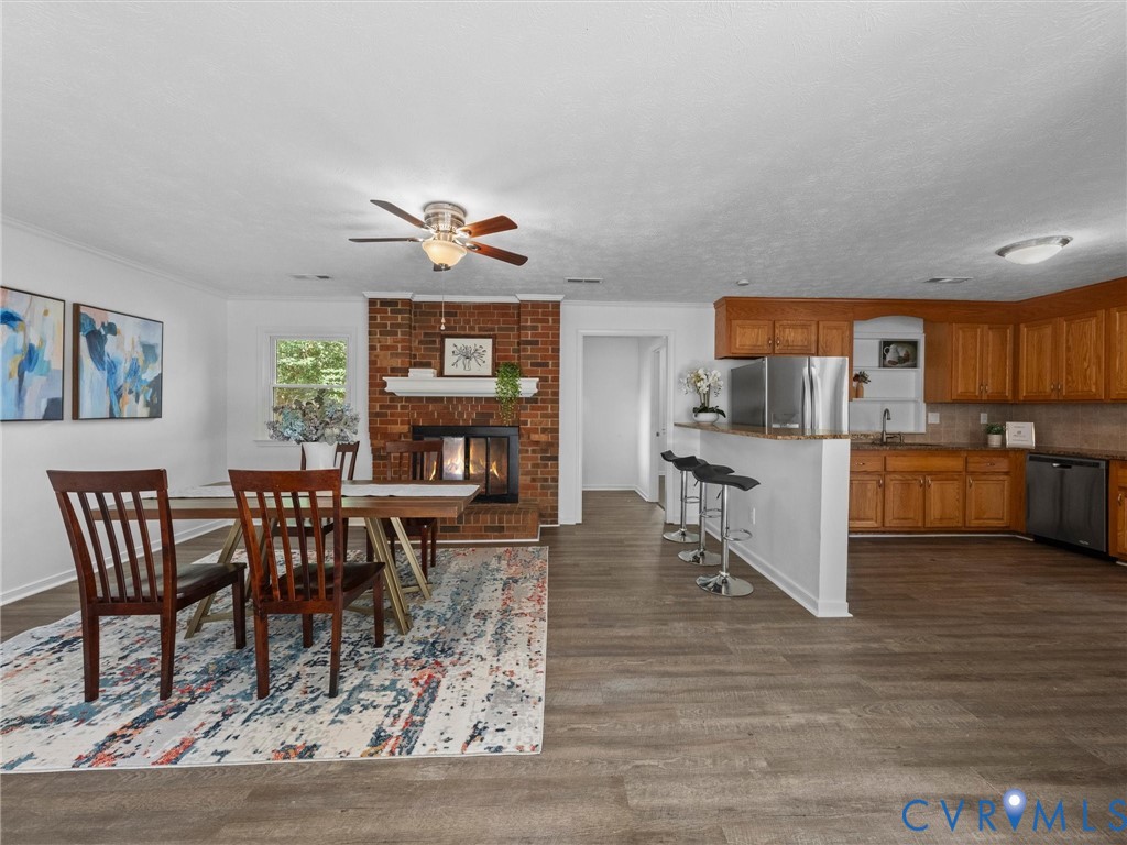 Open concept space featuring wood-finish flooring, a full-height brick fireplace, a kitchen island with a breakfast bar, and wood cabinetry