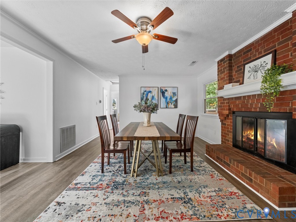 Dining area featuring red brick fireplace, white mantel, wood-finish flooring, and ceiling fan with integrated lighting