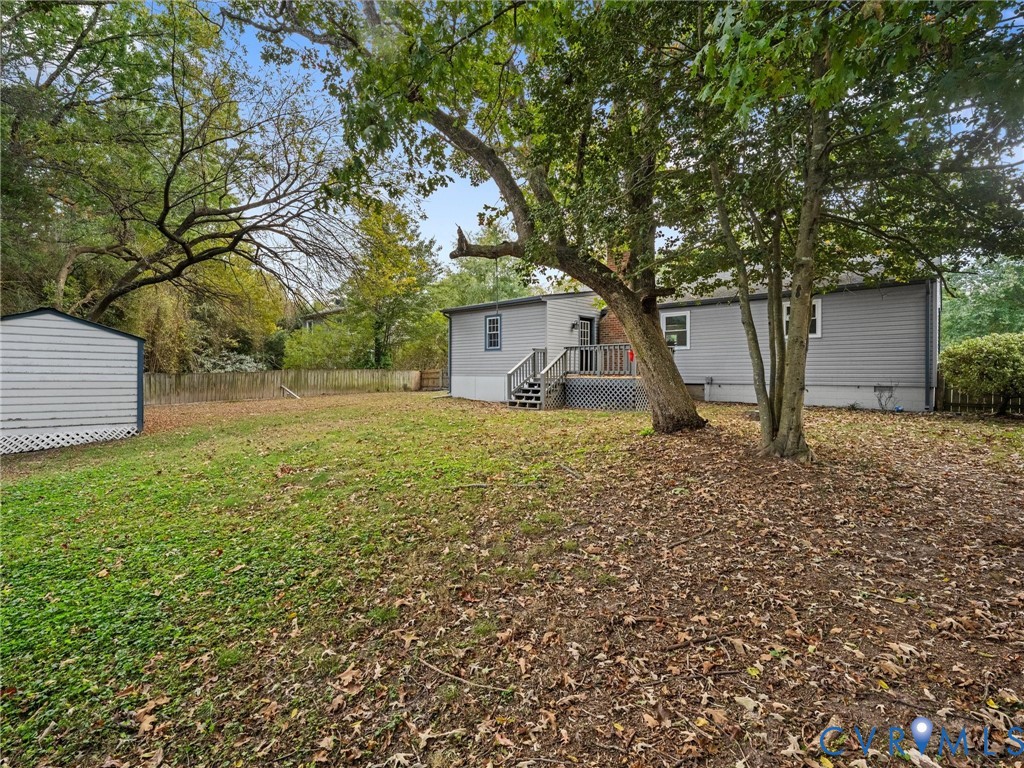 Expansive backyard featuring mature trees, a detached storage structure, wooden rear deck with stairs, and a perimeter wood fence
