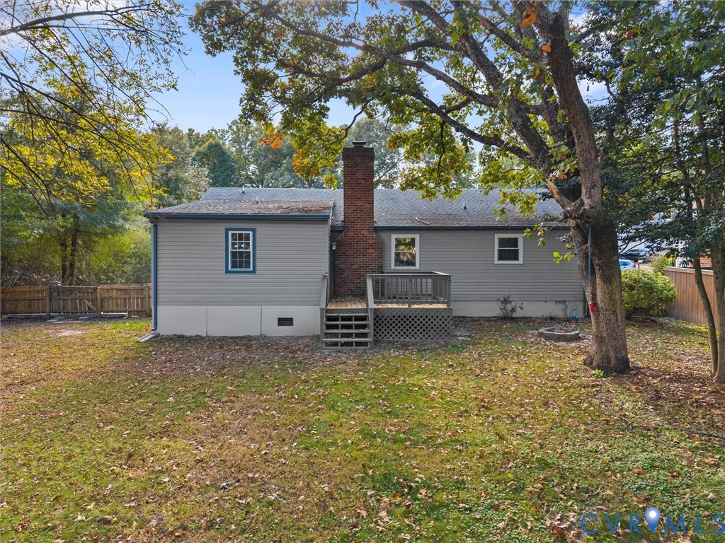 Exterior featuring horizontal siding, a central brick chimney, a wood deck with lattice skirting, and mature trees on a level lot