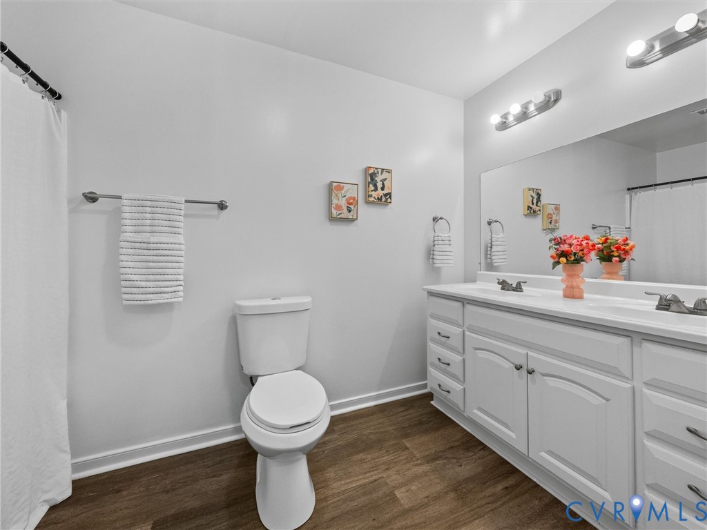 Double-sink vanity with white cabinetry, wood-finish flooring, full-width wall mirror, and dual multi-bulb vanity light fixtures