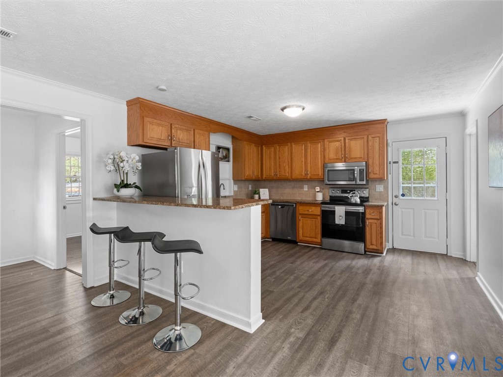 Kitchen featuring wood cabinetry, stone-finish countertops, stainless steel appliances, and wood-finish flooring