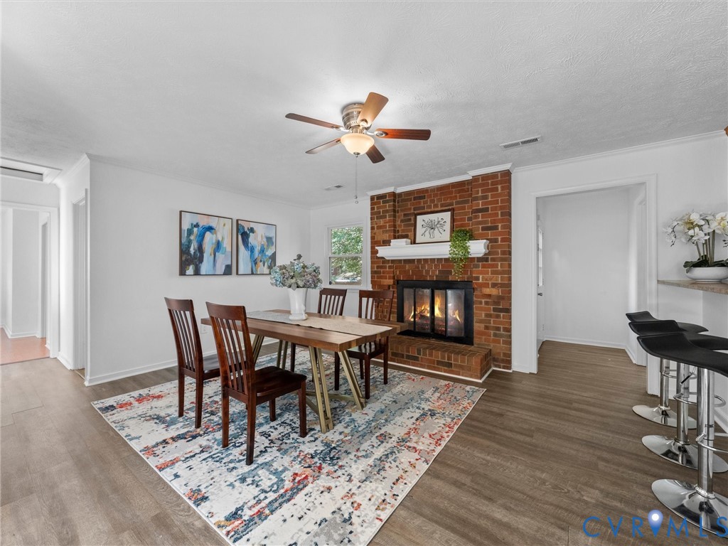 Red brick fireplace with a decorative mantel, wood-finish flooring, and a ceiling-mounted light fixture with a fan