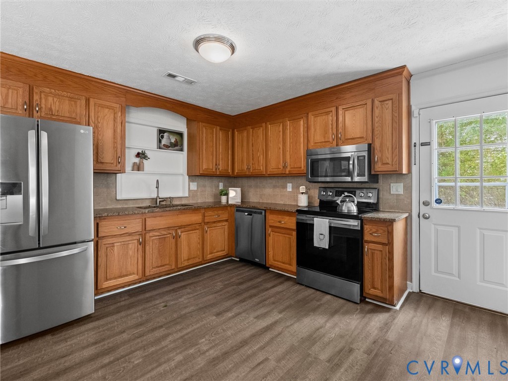 Kitchen featuring wood-finish cabinetry, stone-surface countertops, stainless steel appliances, recessed shelving, and wood-finish flooring