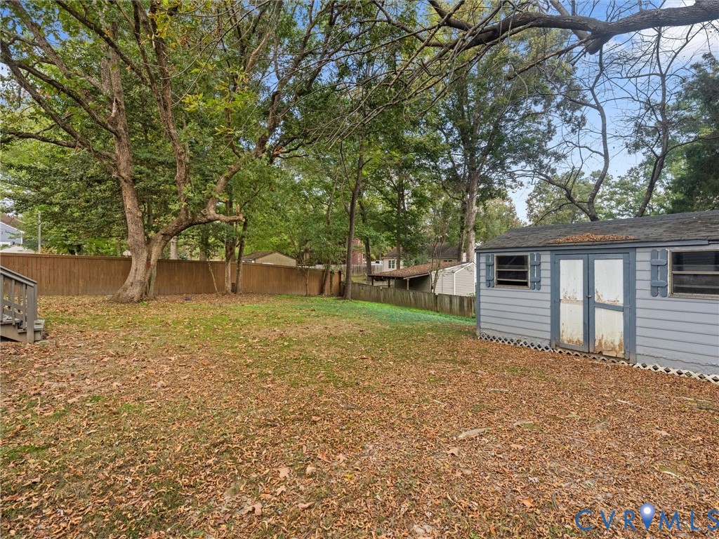 Backyard featuring a wood privacy fence, mature trees, and a detached storage shed with louvered shutters